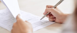 Crop shot of person with pen signing contract at desk in daylight