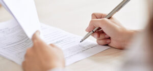 Crop shot of person with pen signing contract at desk in daylight